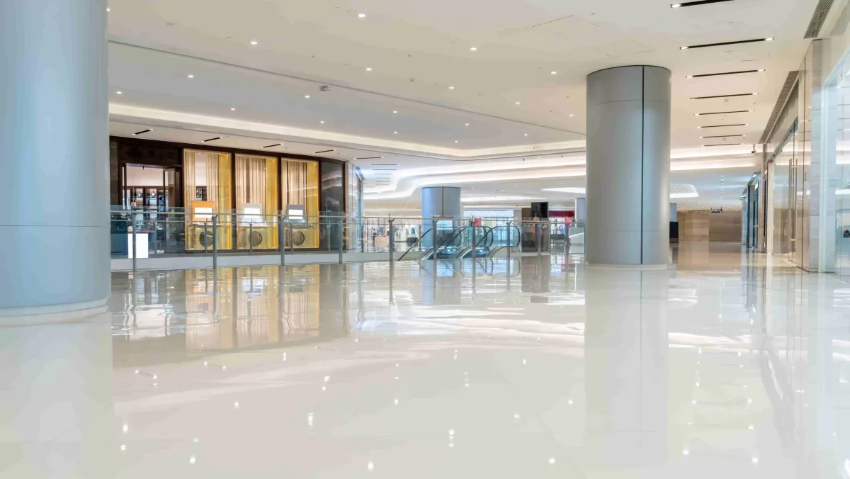A spacious, modern shopping mall interior with glossy white floors, cylindrical columns, glass railings, and escalators.