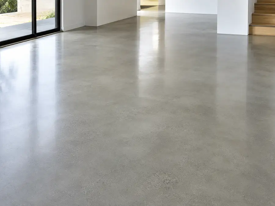 gray-new-concrete Bright modern interior with polished concrete floor, large glass doors, white walls, and wooden stairs on the right.